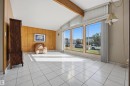 Vaulted ceiling with exposed wood beam, full-height paneled wall, ceramic tile flooring, and a bank of three large windows - 14008 94 Street Nw, Edmonton, AB 
