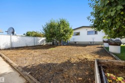 Fenced backyard featuring mature trees, a concrete walkway, and a raised garden bed - 