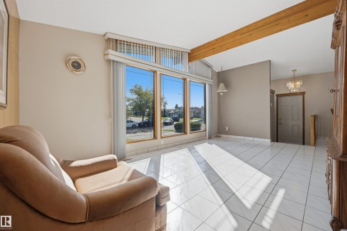 Vaulted ceiling with exposed wood beams, large front-facing windows with upper transom windows, white tile flooring, and a chandelier fixture in the entry - 14008 94 Street Nw, Edmonton, AB 