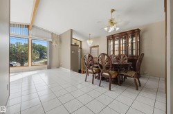 Vaulted ceiling with exposed wood beams, large picture windows, white tile flooring, and a ceiling fan with integrated lighting - 