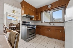 Kitchen featuring wood cabinetry, a stainless steel range with overhead hood, a window over the sink, and white square tile flooring - 