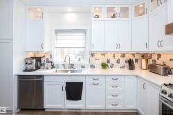 White shaker-style cabinetry with upper glass-front display cabinets, under-cabinet lighting, a patterned backsplash, stainless steel appliances, and a wood-finish flooring - 