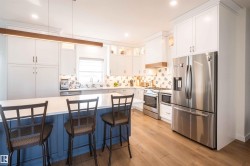 Kitchen featuring a large island with a blue base, white countertops, stainless steel appliances, and light wood-finish flooring - 