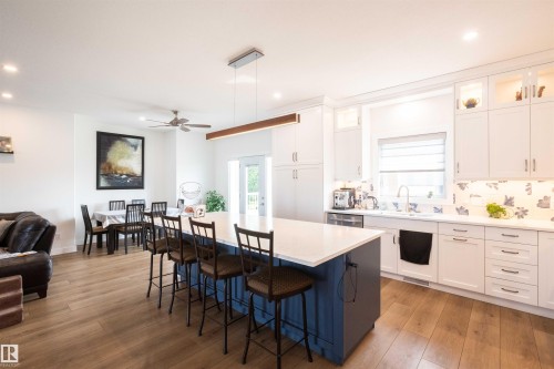 Spacious kitchen featuring a blue island with seating, white cabinetry, integrated lighting, stainless steel sink, and wood-finish flooring - 5404 60Th Street, Barrhead, AB - Indoor