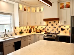 Contemporary kitchen featuring white cabinetry with glass-front upper cabinets, light-toned countertops, and a decorative tile backsplash - 
