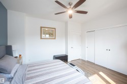 Bright room featuring wood-finish flooring, a ceiling fan with integrated lighting, a white paneled door, and two white sliding closet doors - 