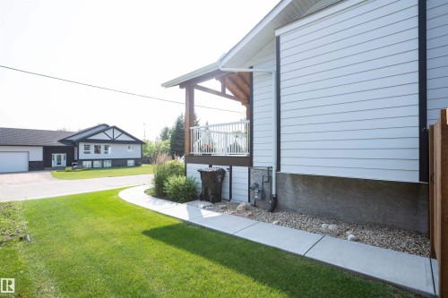 Side exterior featuring white horizontal siding, a covered deck with white railing, and a concrete pathway - 5404 60Th Street, Barrhead, AB - Outdoor With Exterior
