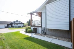 Side exterior featuring white horizontal siding, a covered deck with white railing, and a concrete pathway - 