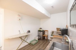 Utility space featuring a stainless steel sink, wood-finish flooring, white walls, and overhead cabinetry - 