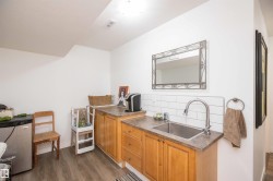 Wet bar area featuring wood-finish cabinetry, a stainless steel sink, and white subway tile backsplash - 