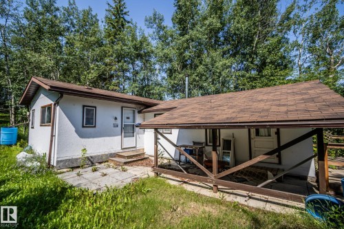 White stucco exterior with a brown shingle roof, featuring a covered porch with a wood railing - 811 59209 Range Rd 95A, Rural St. Paul County, AB - Outdoor