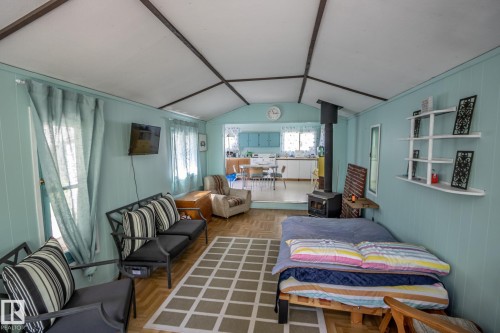 Open-concept living space featuring wood-finish flooring, a contemporary wood-burning stove, paneling on walls, white ceiling with exposed beams, and a glimpse of the kitchen area - 811 59209 Range Rd 95A, Rural St. Paul County, AB - Indoor