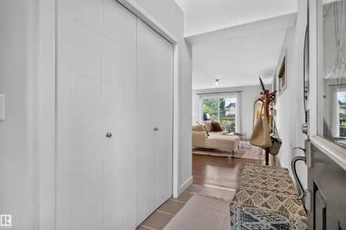 Entryway featuring a built-in closet with paneled doors, tile flooring, and wood-finish flooring extending into the main living area - 5130 Godson Close Nw, Edmonton, AB 
