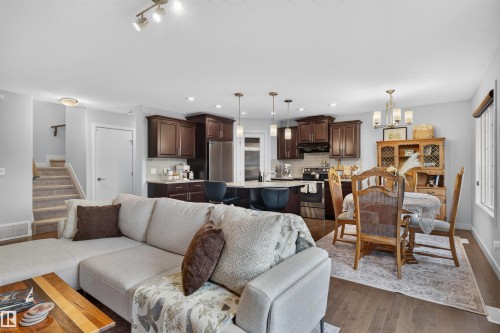 Open-concept living area featuring wood-finish flooring, a kitchen with dark wood cabinetry and stainless steel appliances, and a dining area with a chandelier - 5130 Godson Close Nw, Edmonton, AB 