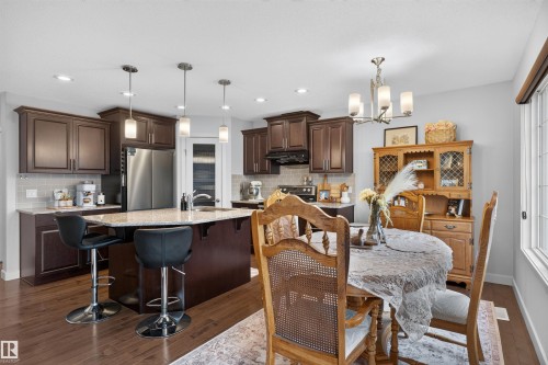 Kitchen featuring dark wood cabinetry, light-toned countertops, stainless steel appliances, and a tile backsplash - 5130 Godson Close Nw, Edmonton, AB 