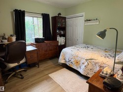 Room featuring wood-finish flooring, a window with black curtains, light green walls, a built-in closet with bi-fold doors, and a wall-mounted shelving unit - 