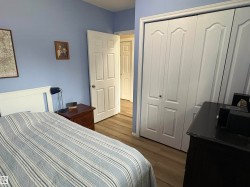 Bedroom featuring wood-finish flooring, light blue walls, a white headboard, and white bi-fold closet doors - 