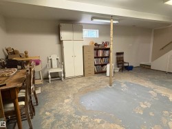 Finished basement area with painted concrete flooring, a small window, built-in cabinetry, fluorescent lighting, and a painted wooden staircase - 