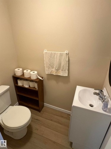 Compact powder room featuring a white pedestal sink, toilet, and wood-finish flooring - 5308 50 St, Ryley, AB 