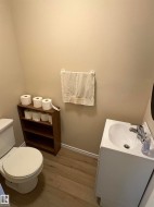 Compact powder room featuring a white pedestal sink, toilet, and wood-finish flooring - 