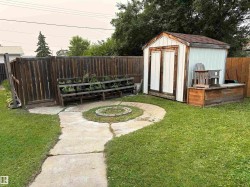Private yard featuring a concrete pathway, a central fire pit, and a storage shed with wood-panel doors - 
