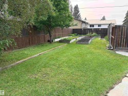 Landscaped backyard featuring a grass lawn, wood fencing, mature trees, and multiple raised garden beds - 