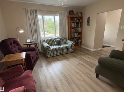 Spacious living area featuring light wood-finish flooring, a bright window with white trim, and neutral wall paint - 