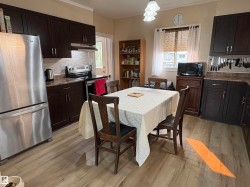 Kitchen featuring dark wood-finish cabinetry, stainless steel appliances, stone-finish countertops, tile backsplash, and light wood-finish flooring - 