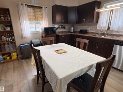 Kitchen featuring dark wood-finish cabinetry, stainless steel dishwasher, light wood-finish flooring, and a tiled backsplash - 