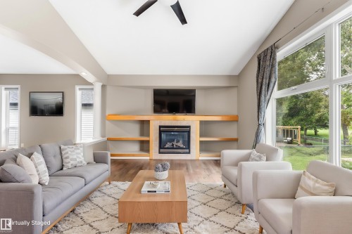 Spacious interior featuring wood-finish flooring, a contemporary fireplace with built-in shelving, vaulted ceilings, and large picture windows - 2060 Brennan Crescent Nw, Edmonton, AB 