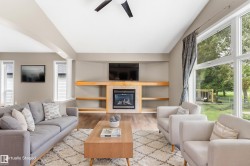 Spacious interior featuring wood-finish flooring, a contemporary fireplace with built-in shelving, vaulted ceilings, and large picture windows - 