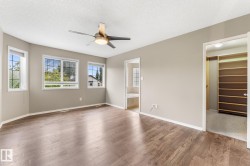 Wood-finish flooring, three windows with blinds, ceiling fan with integrated lighting, built-in closet shelving, and a separate doorway to a bathroom with a built-in tub - 
