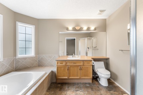Soaking tub with tiled surround, wood-finish vanity with countertop, and a glass-enclosed shower - 2060 Brennan Crescent Nw, Edmonton, AB 