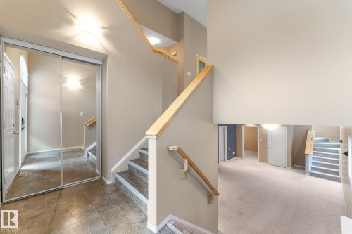 Foyer with tile flooring, mirrored closet doors, and a multi-level staircase with wood railings - 2060 Brennan Crescent Nw, Edmonton, AB 