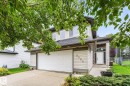 Two-story residence featuring light-toned siding, dark roof shingles, an attached garage, a paved driveway, and a covered entry - 2060 Brennan Crescent Nw, Edmonton, AB 