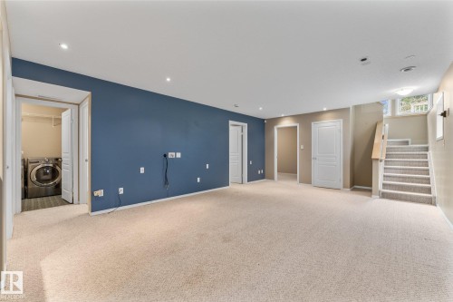 Expansive carpeted area with recessed lighting, a dedicated laundry area, and a staircase with a wood handrail - 2060 Brennan Crescent Nw, Edmonton, AB 
