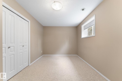 Carpeted flooring, neutral wall paint, white trim, window with roller blind, and white bi-fold closet doors - 2060 Brennan Crescent Nw, Edmonton, AB 