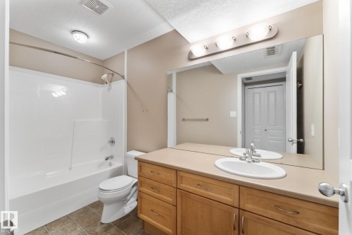 Bathroom featuring a built-in wood-finish vanity with an integrated sink, a large wall-mounted mirror, a tub/shower combination, and tiled flooring - 2060 Brennan Crescent Nw, Edmonton, AB 