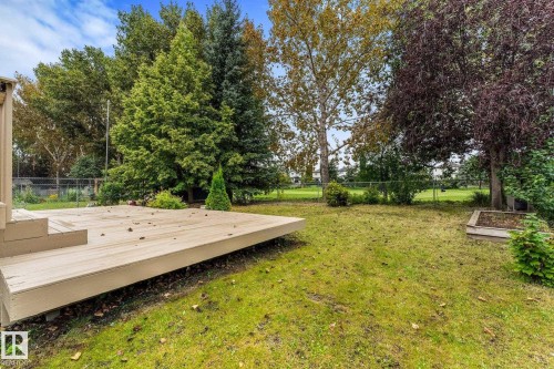 Expansive rear yard featuring a large wood-finish deck, mature trees, manicured lawn, and raised garden bed - 2060 Brennan Crescent Nw, Edmonton, AB 