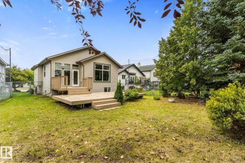 Expansive backyard featuring a wood deck with steps, mature trees, and a manicured lawn - 2060 Brennan Crescent Nw, Edmonton, AB 