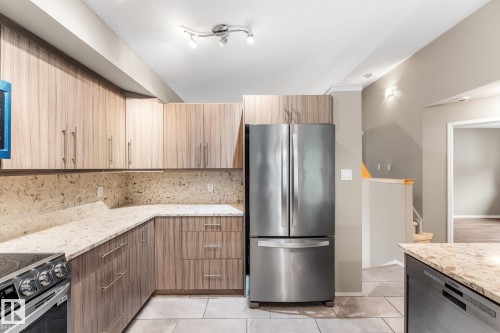 Modern kitchen featuring wood-finish cabinetry, light-toned countertops, and a full stainless steel appliance suite - 2060 Brennan Crescent Nw, Edmonton, AB 