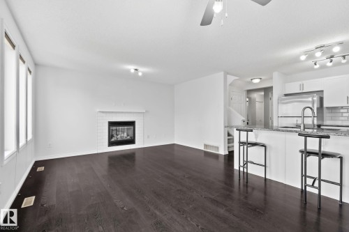 Wood-finish flooring throughout, with a tiled fireplace and white mantel - 9523 Simpson Crest Nw, Edmonton, AB 