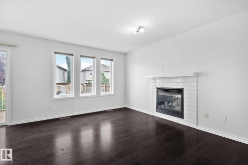 Dark wood-finish flooring, white walls, and a white subway tile fireplace with a mantel - 9523 Simpson Crest Nw, Edmonton, AB 