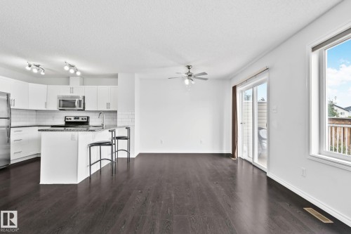 Open-concept living area with dark wood-finish flooring, white walls, and a ceiling fan - 9523 Simpson Crest Nw, Edmonton, AB 