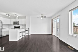 Open-concept living area with dark wood-finish flooring, white walls, and a ceiling fan - 