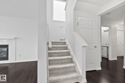 Carpeted staircase with white railings, dark wood-finish flooring, and a fireplace with white brick surround - 