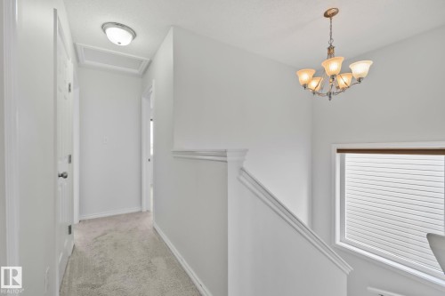 Staircase featuring a decorative chandelier and window with blinds, complementing the light-colored carpeting and white walls in the hallway - 9523 Simpson Crest Nw, Edmonton, AB 