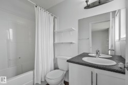 Bathroom featuring a white bathtub, toilet, and a vanity with a dark-finish countertop, two oval sinks, and a chrome faucet - 
