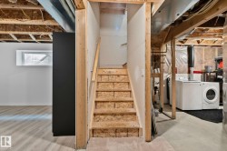 Unfinished basement featuring a wood staircase with wood handrail, exposed joists, and a partial finished area with light wood-finish flooring and a horizontal window - 