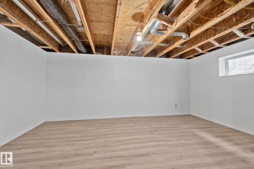 Unfinished ceiling with exposed joists and ductwork, white painted walls, wood-finish flooring, and a single window with blinds - 9523 Simpson Crest Nw, Edmonton, AB 